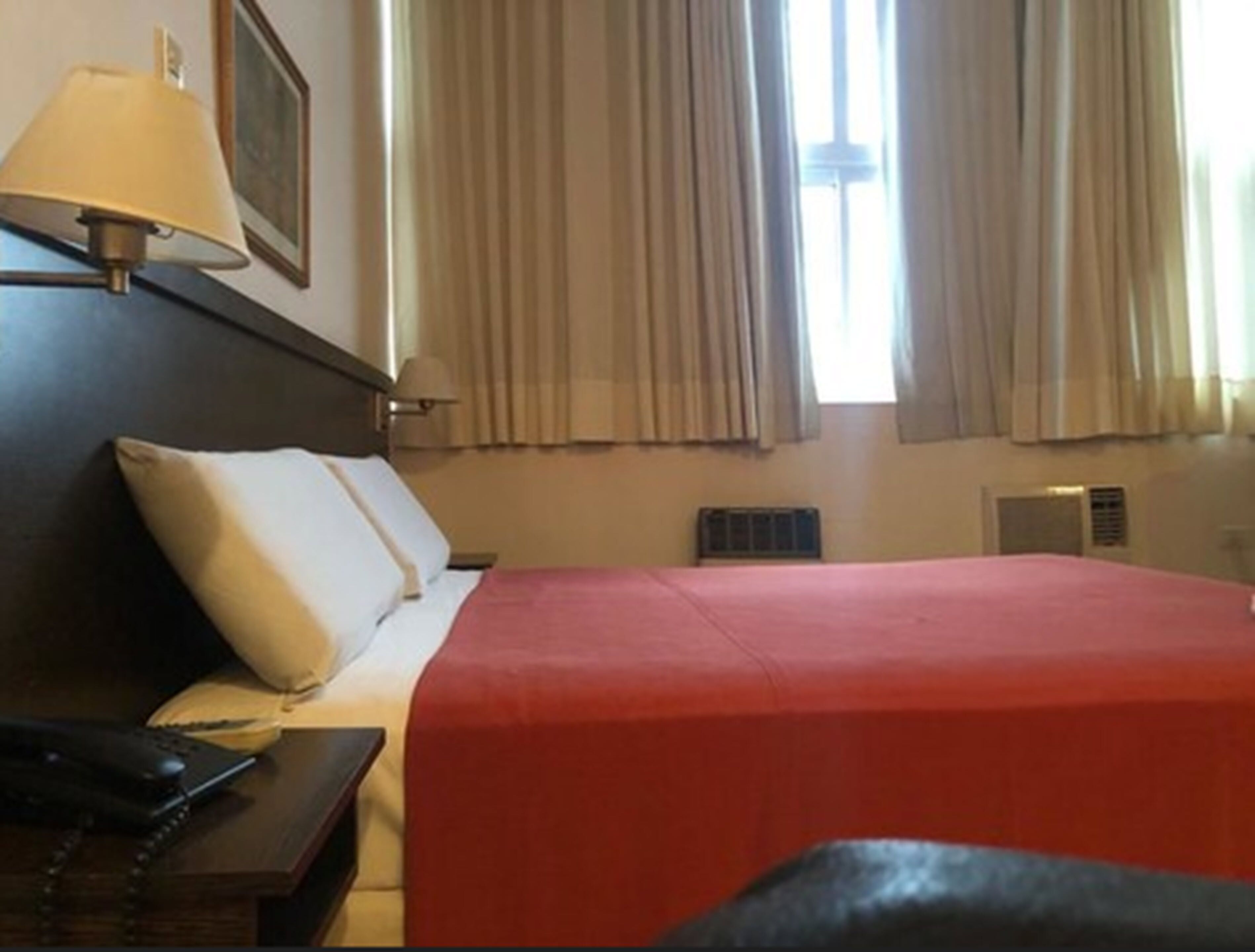 Una camera d'albergo con un letto, un comodino, una lampada e una finestra con tende.
