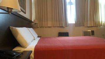 Una camera d'albergo con un letto, un comodino, una lampada e una finestra con tende.