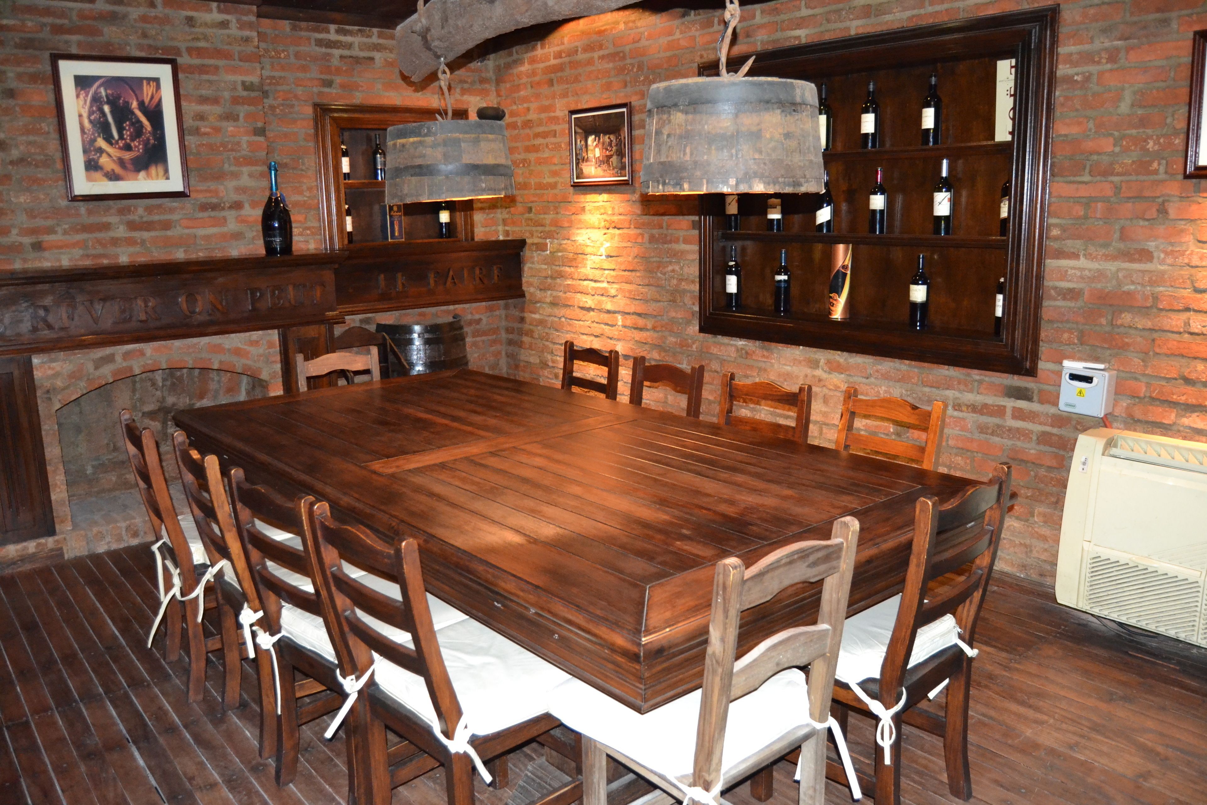 A wooden dining table with chairs, a brick wall, and a wine rack with bottles.
