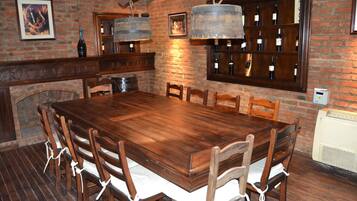 A wooden dining table with chairs, a brick wall, and a wine rack with bottles.