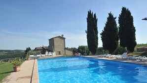 A swimming pool with lounge chairs, a stone building, and tall cypress trees. - Country House Santa Felicita la Paterna (Città di Castello)