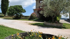 A stone building with a gravel driveway, surrounded by a garden with various flowers and a tall tree. - Country House Santa Felicita la Paterna (Città di Castello)