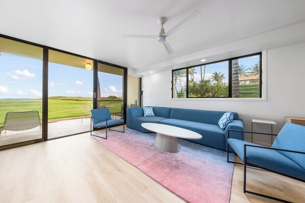 A modern living room with a blue sofa, a coffee table, and a view of a green field through large windows.