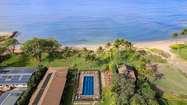 An aerial view of a resort with a swimming pool, palm trees, and a beach.