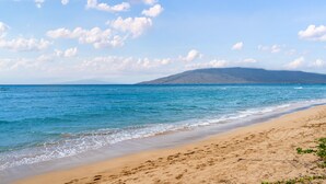 A beach with clear blue water, sandy shore, and a distant mountain.