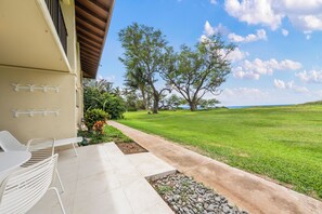 Un patio con mobiliario exterior, un sendero que conduce a un área con césped y árboles al fondo.