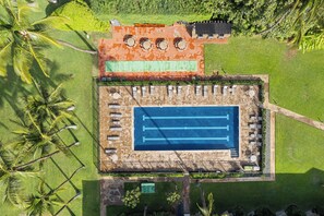 Vista aérea de un complejo turístico con piscina, tumbonas y cancha de tenis.