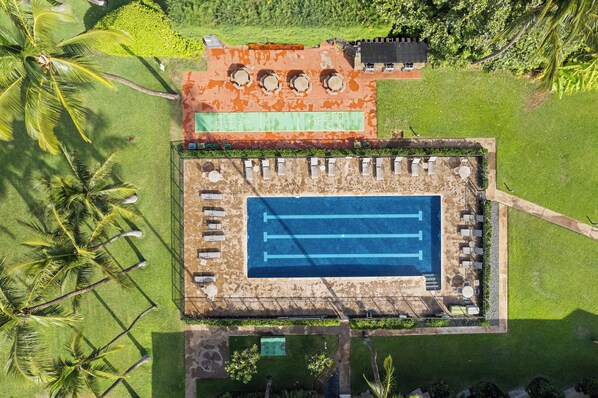 Vista aérea de un complejo turístico con piscina, tumbonas y cancha de tenis.