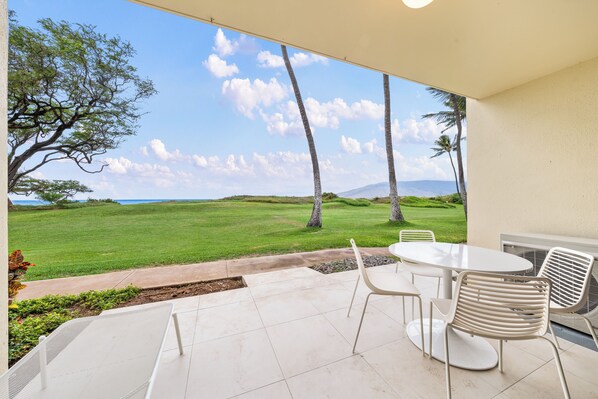 Un patio con una mesa y sillas, con vista a un área verde con árboles y una lejana vista de montañas.