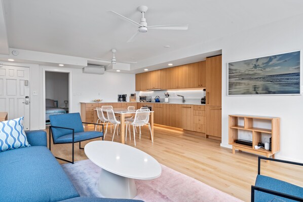 A modern living room with a white coffee table, blue sofas, and a dining area with a white table and chairs.