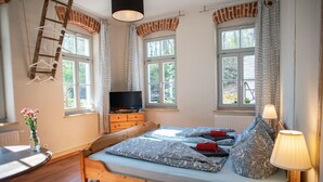 Une chambre à coucher avec un lit en bois, une commode, un téléviseur et une fenêtre avec des rideaux.