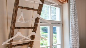 Une échelle en bois rustique, avec des supports blancs, est adossée à un mur de briques près d’une fenêtre.