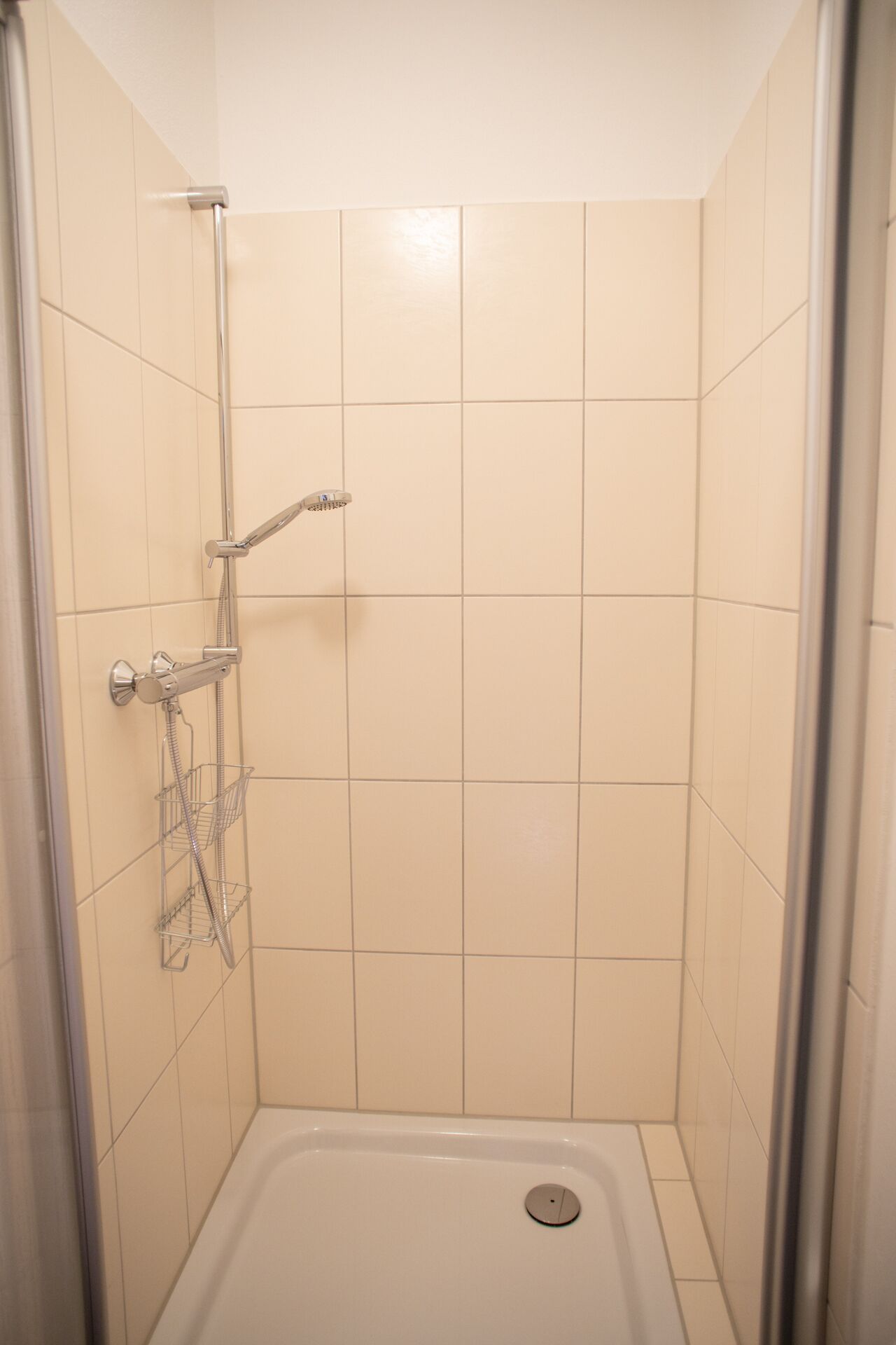 Un espacio de ducha pequeño y cerrado, con un cabezal de ducha y un estante metálico.