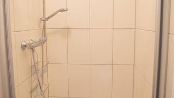 Un espacio de ducha pequeño y cerrado, con un cabezal de ducha y un estante metálico.