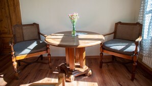 Une table ronde en bois, accompagnée de deux chaises rembourrées, un vase avec des fleurs et un rideau à motifs.
