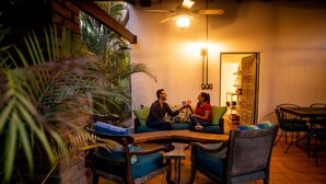 Un espacio interior acogedor con mesa y sillas de madera, rodeado de plantas en macetas y un piso de baldosas.