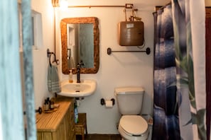 Un baño con tocador de madera, lavamanos, espejo, inodoro y cortina de ducha.