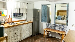 Cocina compacta con refrigerador, pileta y encimera de madera. Un banco se encuentra cerca de una ventana con cortinas azules.