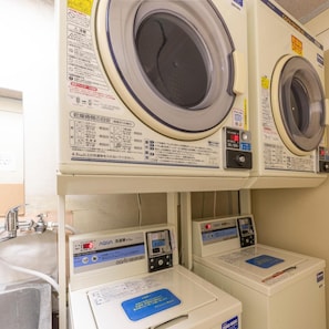 A laundry facility with two washing machines and two dryers, each with control panels and safety instructions.