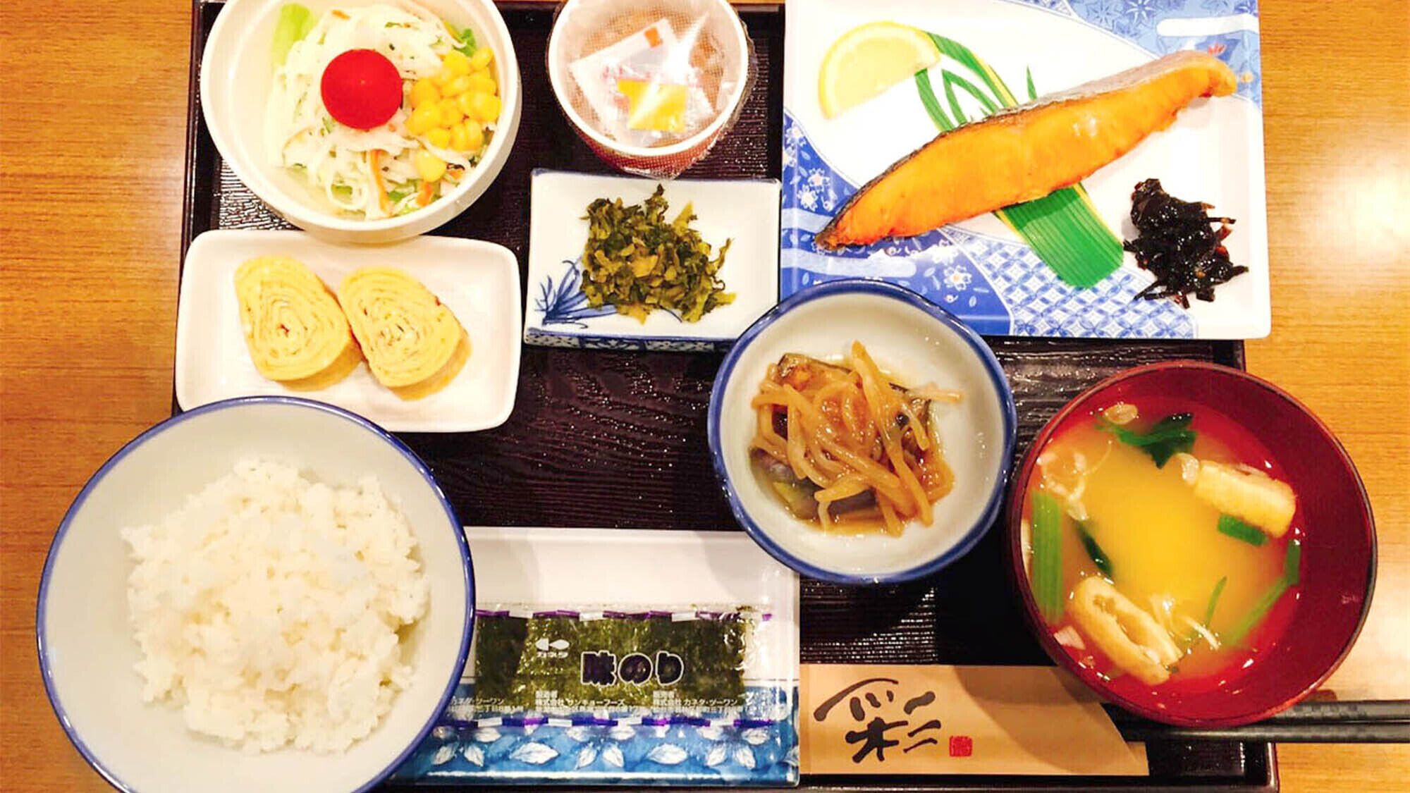 A variety of Japanese dishes including sushi, tempura, and a bowl of soup, arranged on a wooden table.