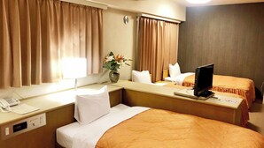 Ein Hotelzimmer mit zwei Betten, einem Schreibtisch mit Telefon, einem Fernseher und einer Vase mit Blumen.