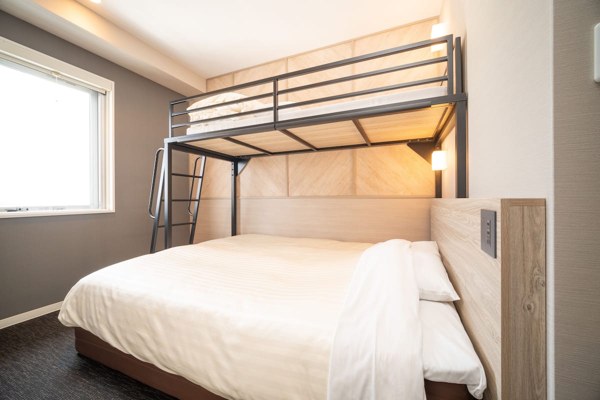A bunk bed with a ladder, a window, and a wall-mounted light fixture.