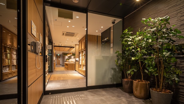 A hotel corridor with wooden flooring, a reception area, and potted plants.