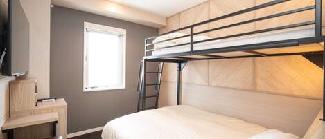 A bunk bed room with a desk and chair, a window, and a flat-screen TV mounted on the wall.