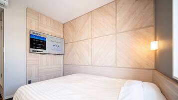 Una habitación de hotel con una cama, un televisor empotrado mostrando información de la habitación y una lámpara.