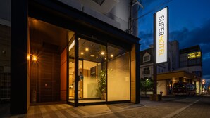A hotel entrance with a glass facade, a visible indoor plant, and a bus stop outside.