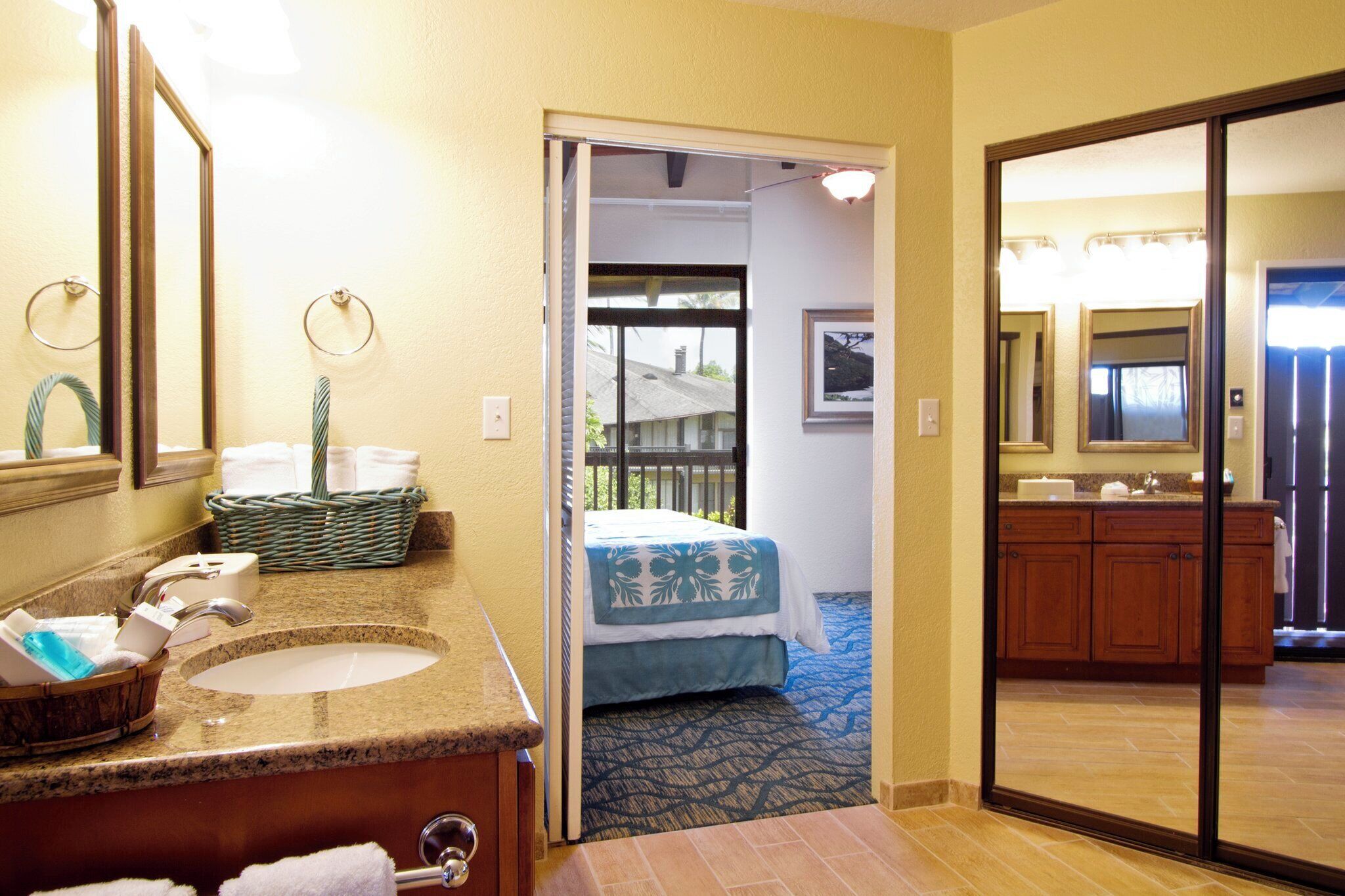 A hotel bathroom with a sink, mirror, and a view of the bedroom through an open door.
