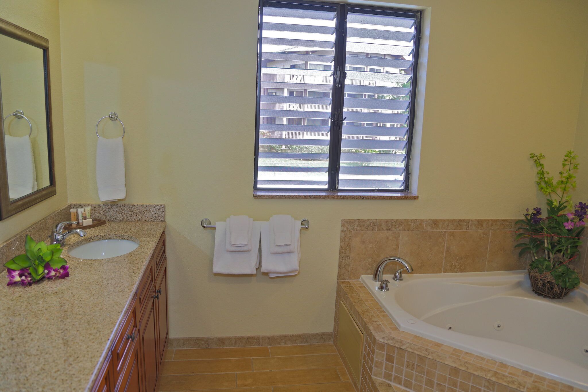A bathroom with a sink, mirror, and bathtub. There are towels hanging on the wall and a window with blinds.