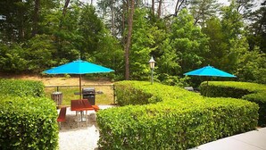 A patio area with two blue umbrellas, a barbecue grill, and neatly trimmed hedges. - Laurel Crest Vacation Resort in the Smoky Mountains. (Pigeon Forge)