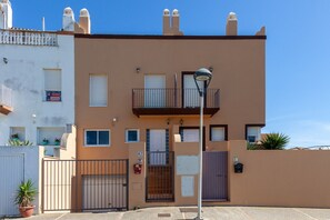 A two-story residential building with a balcony, a gated entrance, and a clear blue sky.