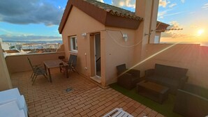 Eine Dachterrasse mit Tisch und Stühlen, einer kleinen Sitzecke und Blick auf die Stadt.