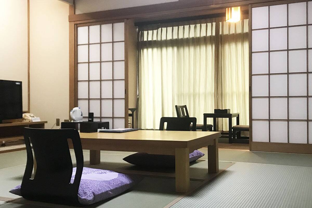 Une pièce de style japonais traditionnel, avec un sol recouvert de tatamis, une table basse, des chaises, un téléviseur et des portes coulissantes.