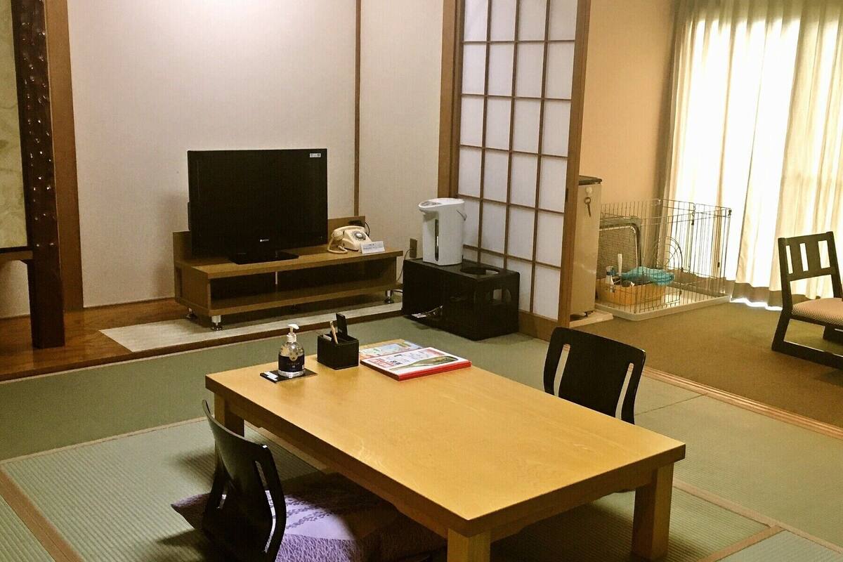 Une pièce de style japonais traditionnel, avec un sol recouvert de tatamis, une petite table en bois, un téléviseur et une porte coulissante donnant sur un balcon.