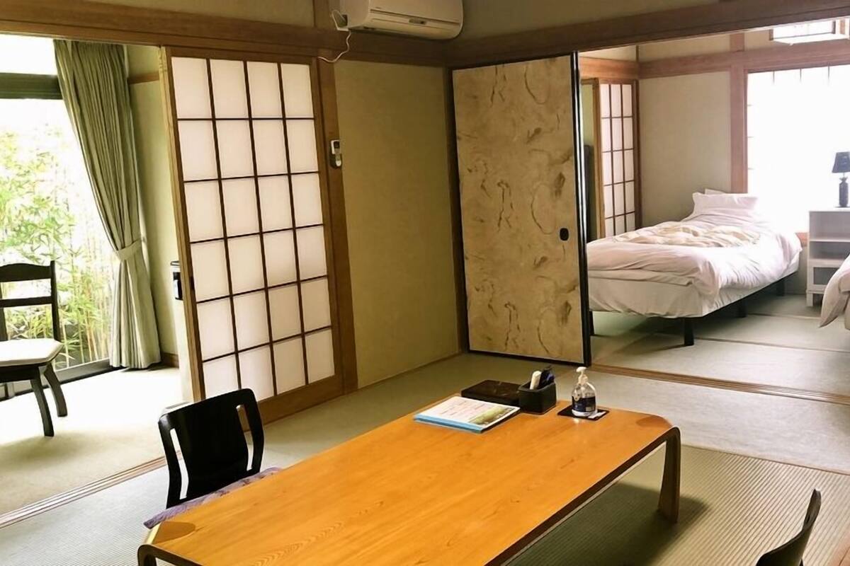 Une pièce de style japonais traditionnel, avec un sol recouvert de tatamis, un bureau en bois, une chaise et un lit recouvert d’une courtepointe blanche.