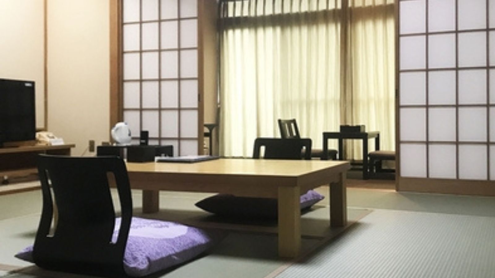 A traditional Japanese room with tatami flooring, a low table, and black chairs.