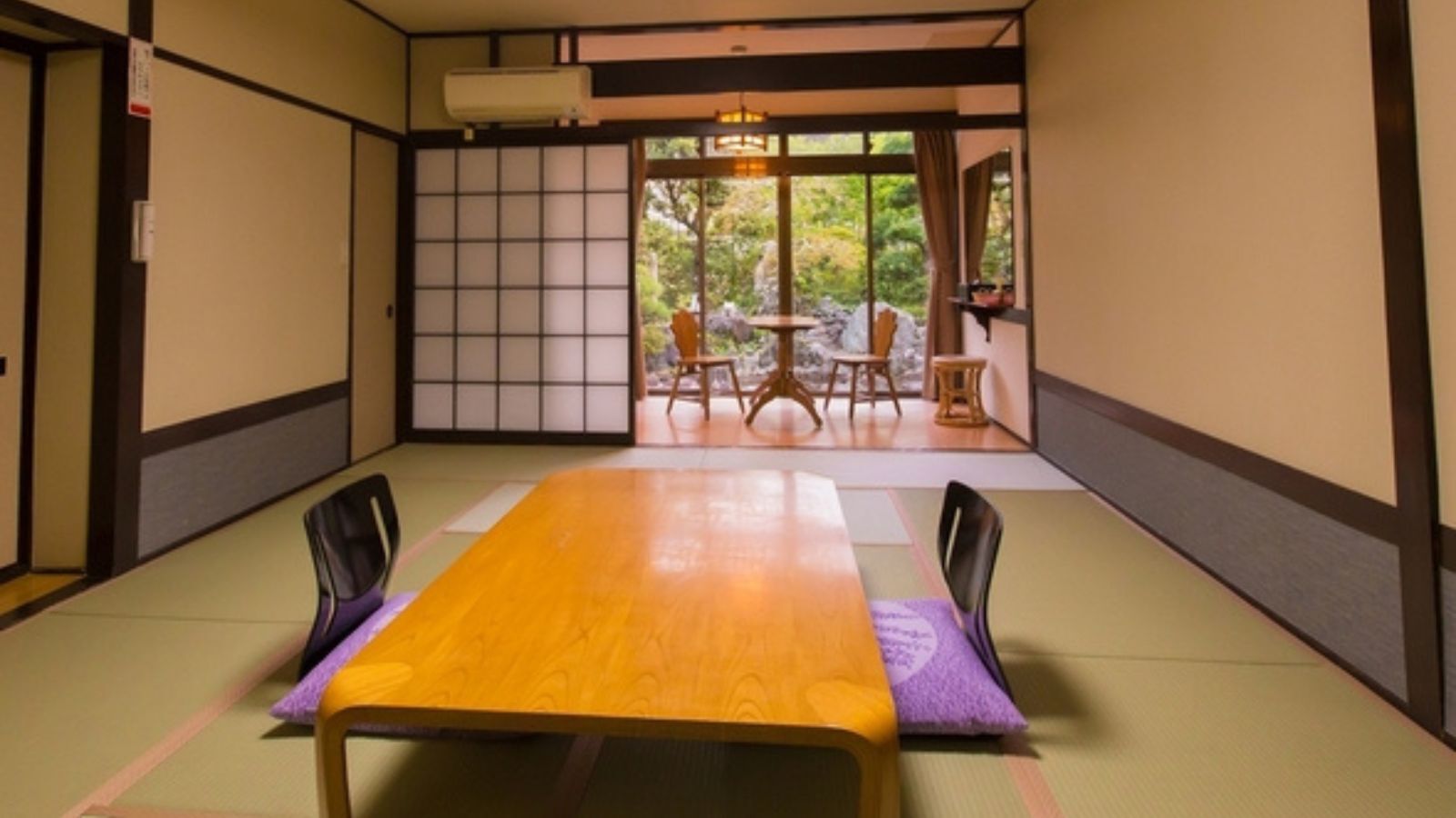 A traditional Japanese room with tatami flooring, a wooden table, and sliding doors leading to an outdoor garden.
