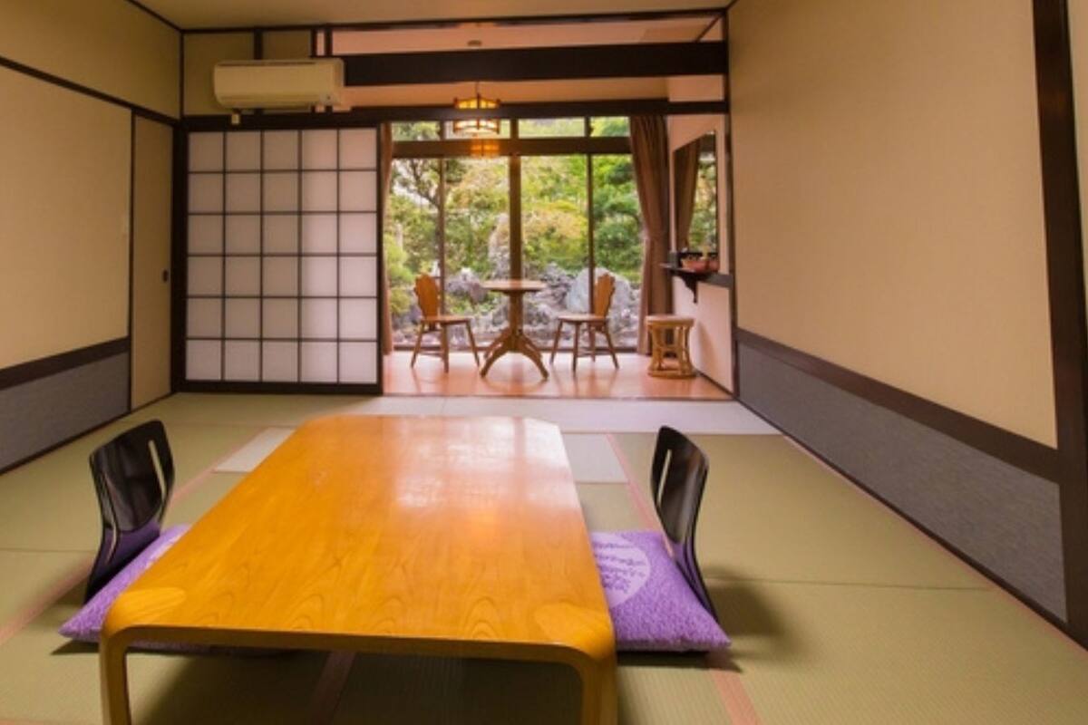 Une pièce de style japonais traditionnel, avec un sol recouvert de tatamis, une table en bois et des portes coulissantes donnant sur un jardin extérieur.