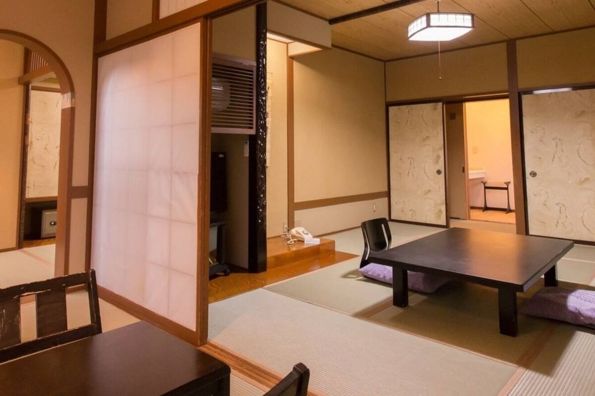 Une pièce de style japonais traditionnel, avec un sol recouvert de tatamis, une table basse, une chaise et des portes coulissantes.