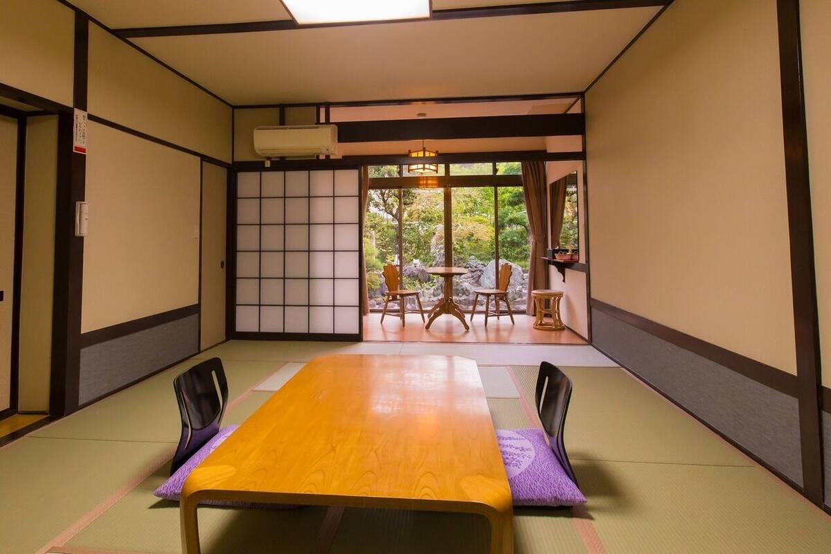 Une pièce de style japonais traditionnel, avec un sol recouvert de tatamis, une table en bois et une vue sur un jardin extérieur.