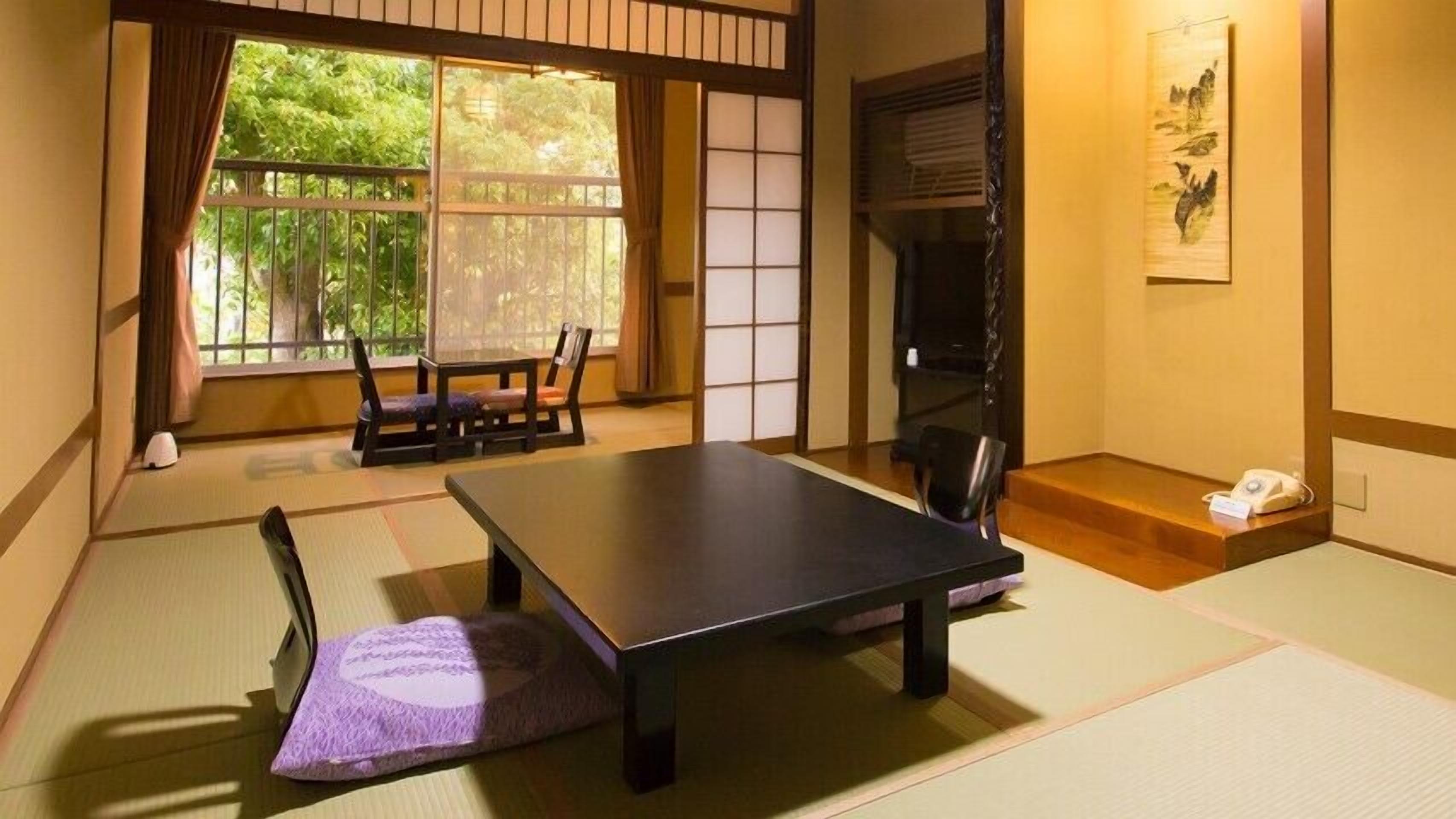 A tatami mat room with a low table, a chair, a futon, and a sliding door.