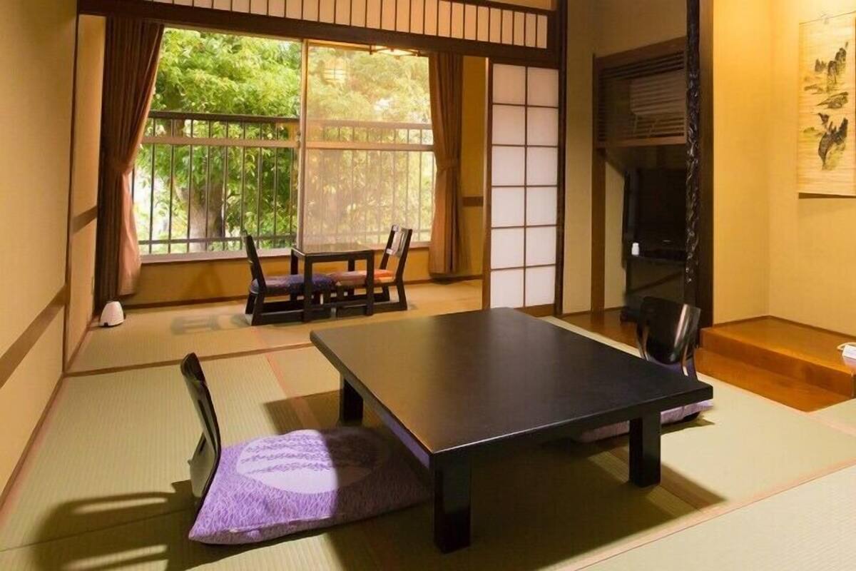 Une pièce avec un sol recouvert de tatamis, une petite table basse, une chaise, un futon et une porte coulissante.