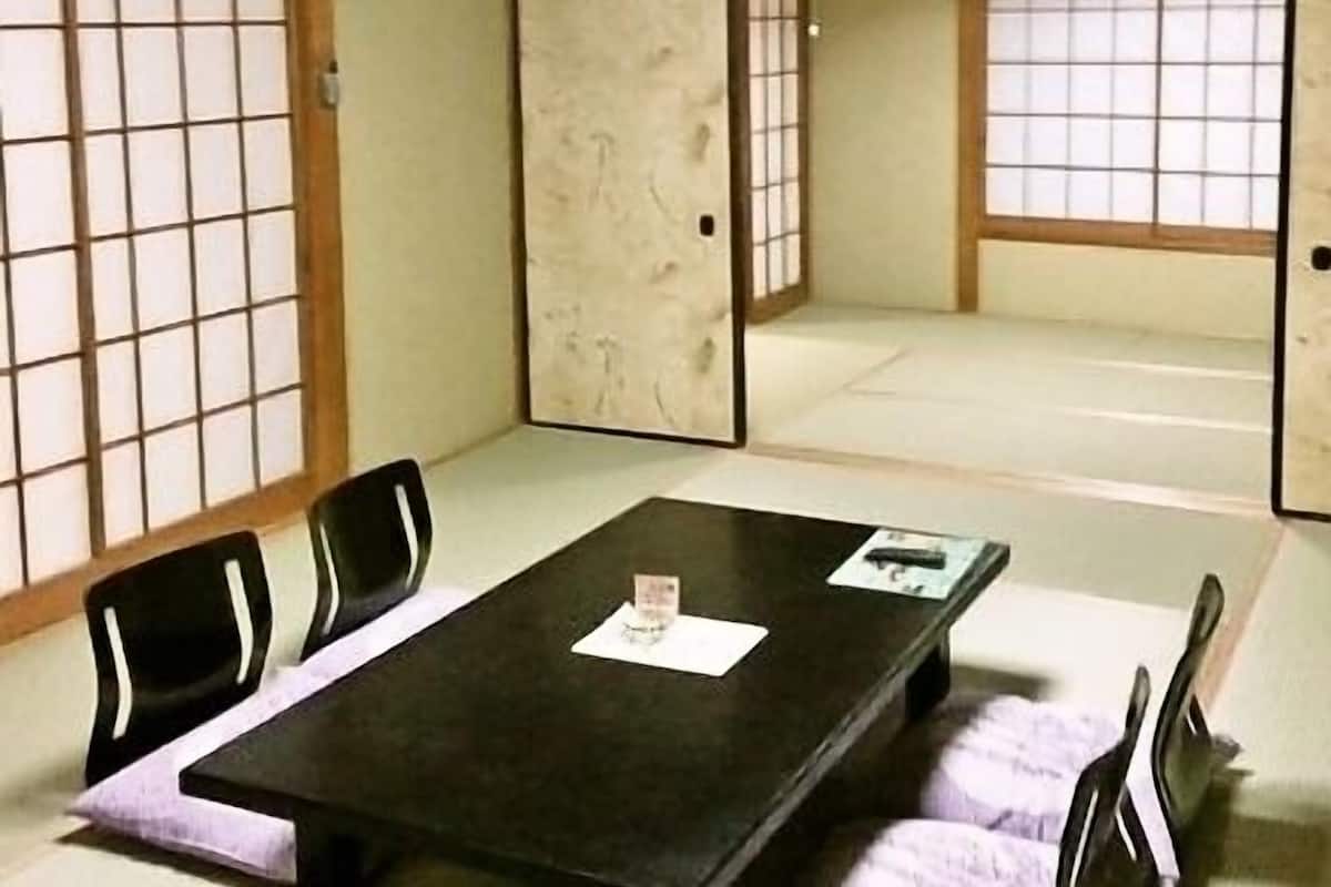 Une pièce de style japonais traditionnel, avec un sol recouvert de tatamis, des paravents en papier de riz (shoji) et une petite table basse entourée de chaises.