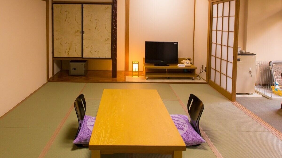 A traditional Japanese room with tatami flooring, a low table with chairs, a television, and a sliding door.