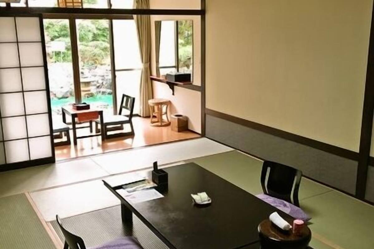 Une pièce de style japonais traditionnel, avec un sol recouvert de tatamis, une petite table basse avec un coussin et des portes coulissantes donnant sur un espace extérieur.