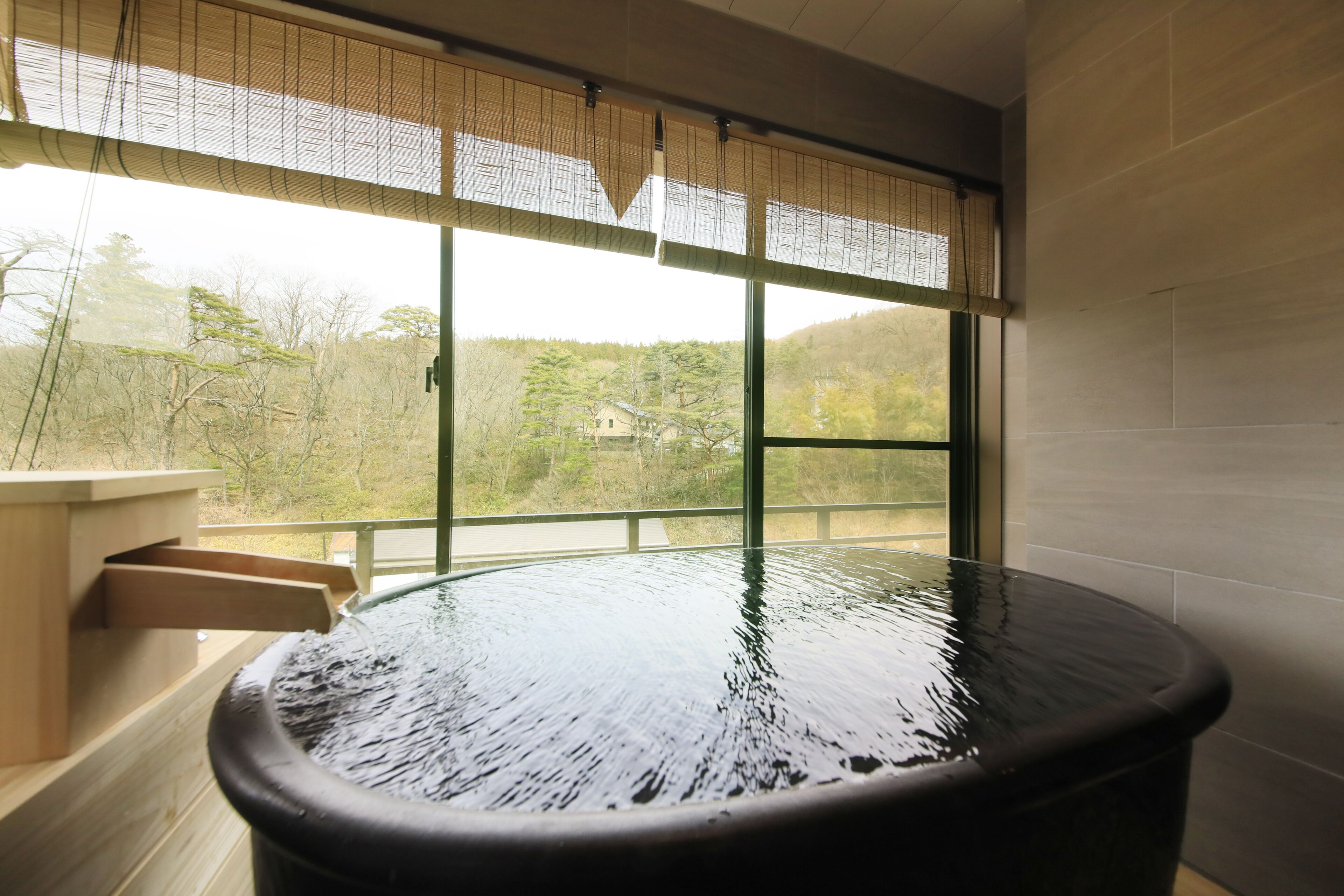 A hot spring bath with a view of trees and hills through large windows.