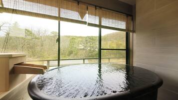 A hot spring bath with a view of trees and hills through large windows.
